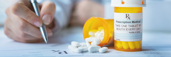 Medicare Part D: A hand signs a medical form with prescription pill bottles and spilled white tablets, representing medication, health, and pharmaceutical care.